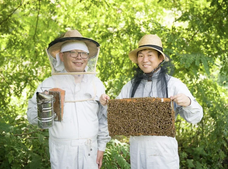 巣枠を手に緑の中に立つ板垣養蜂園の2人